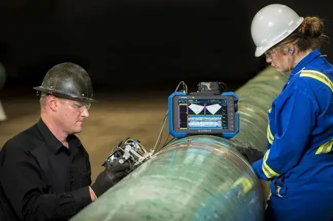 Dos inspectores de campo a pie de obra realizando el escaneo de soldaduras de tuberías de gran diámetro. Utilizan un escáner automatizado conectado al detector de fallas OmniScan X4, el cual muestra datos de la inspección Phased Array en tiempo real sobre la tubería.